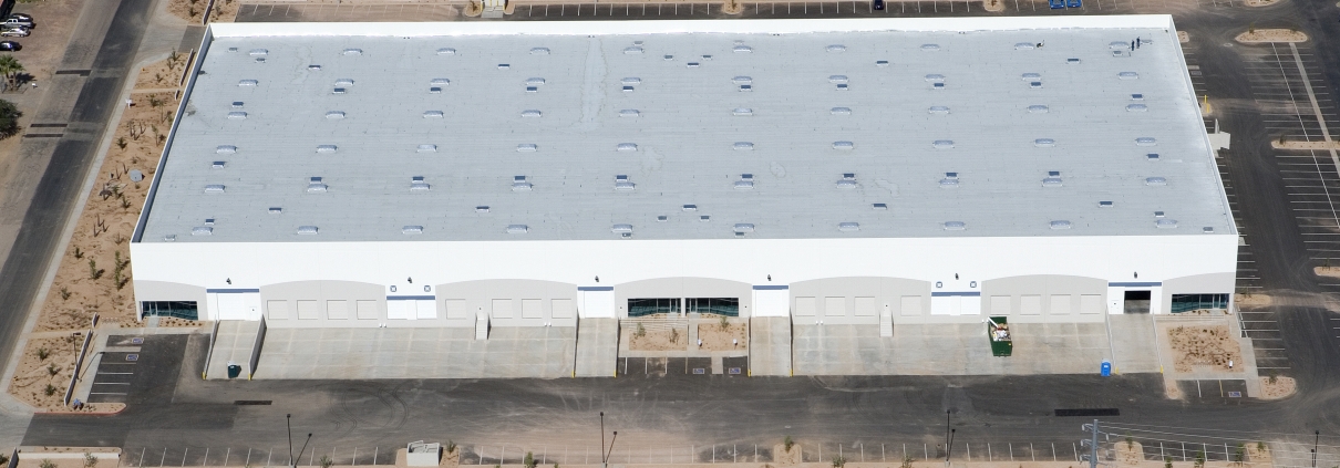 Aerial view of a large white warehouse building with a flat roof in an industrial area