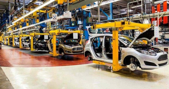 Automobile assembly line with partially assembled cars and robotic manufacturing equipment in a modern factory